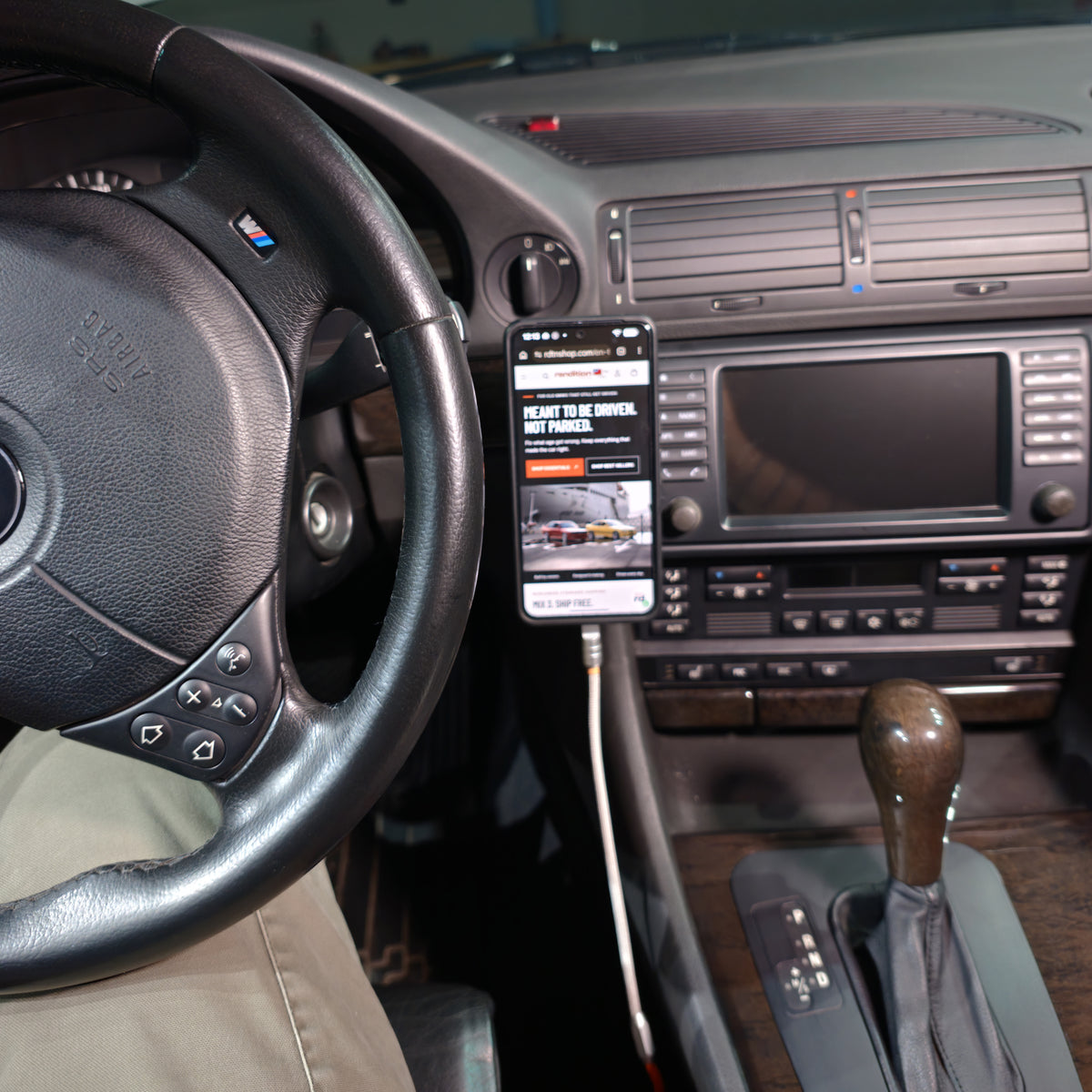 Wide BMW E38 interior view with the phone mounted beside the center display and a cable connected directly to the phone.